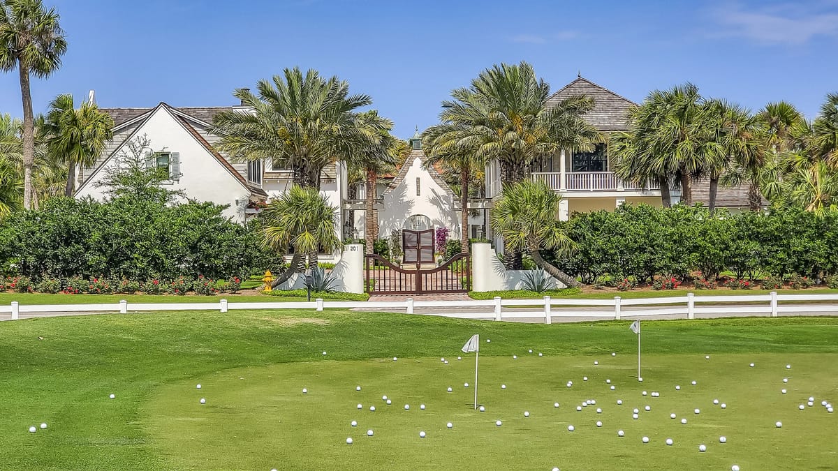 Exterior front view of a property with manicured lawn, putting green, palm trees, and two white buildings.