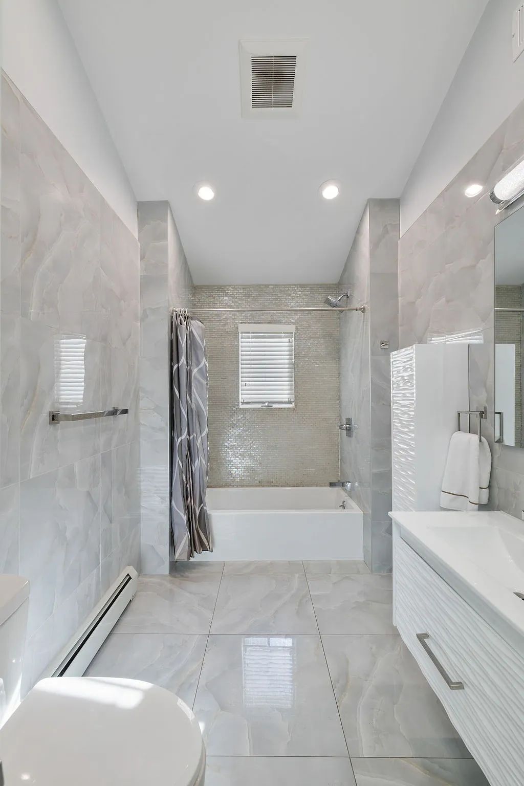 Bathroom with freestanding bathtub, wall-mounted sink, glass shower, and light gray tiled walls and floor.