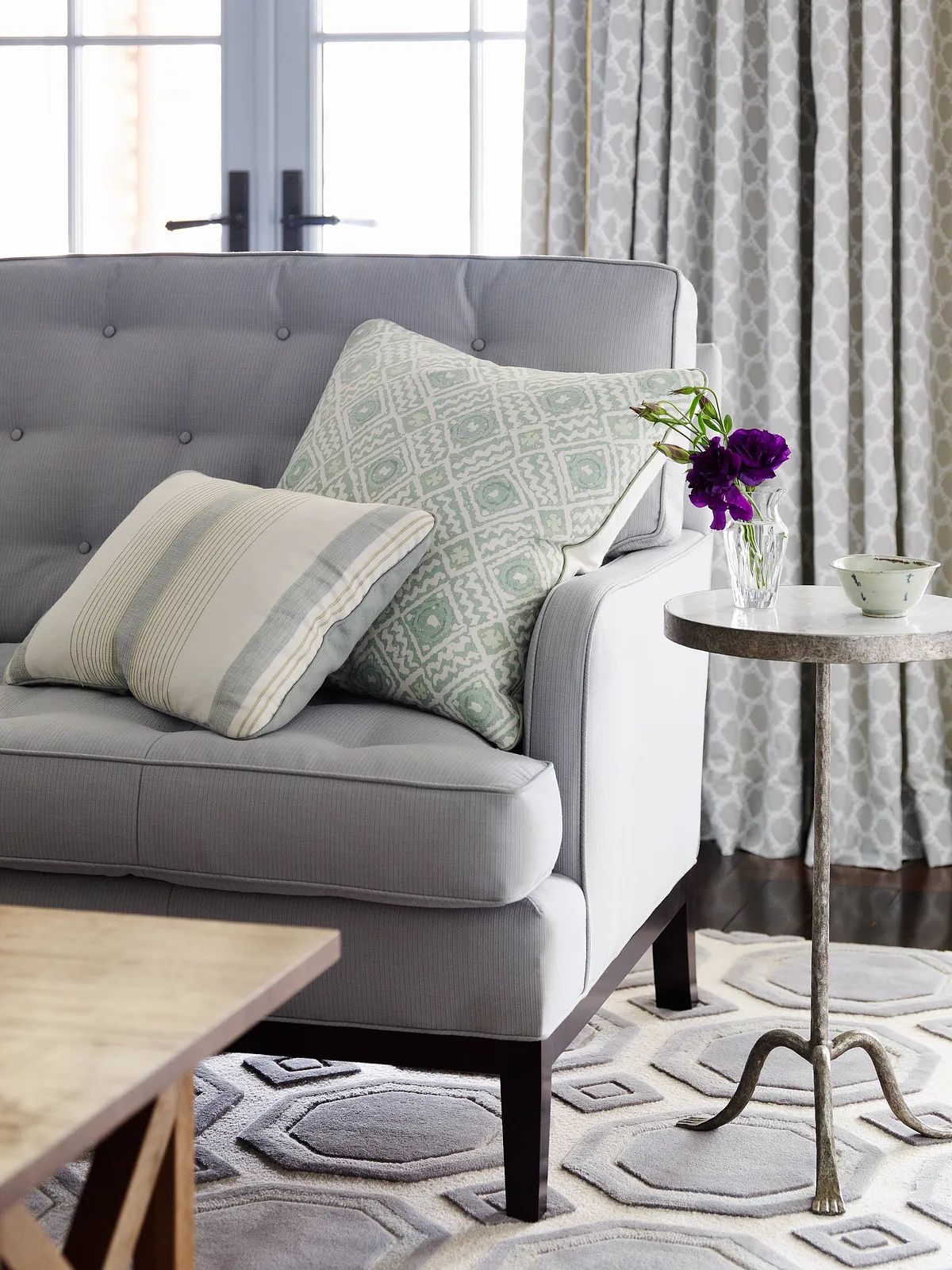 Living room with gray sofa, round side table, patterned rug, and window with drapes providing natural light.