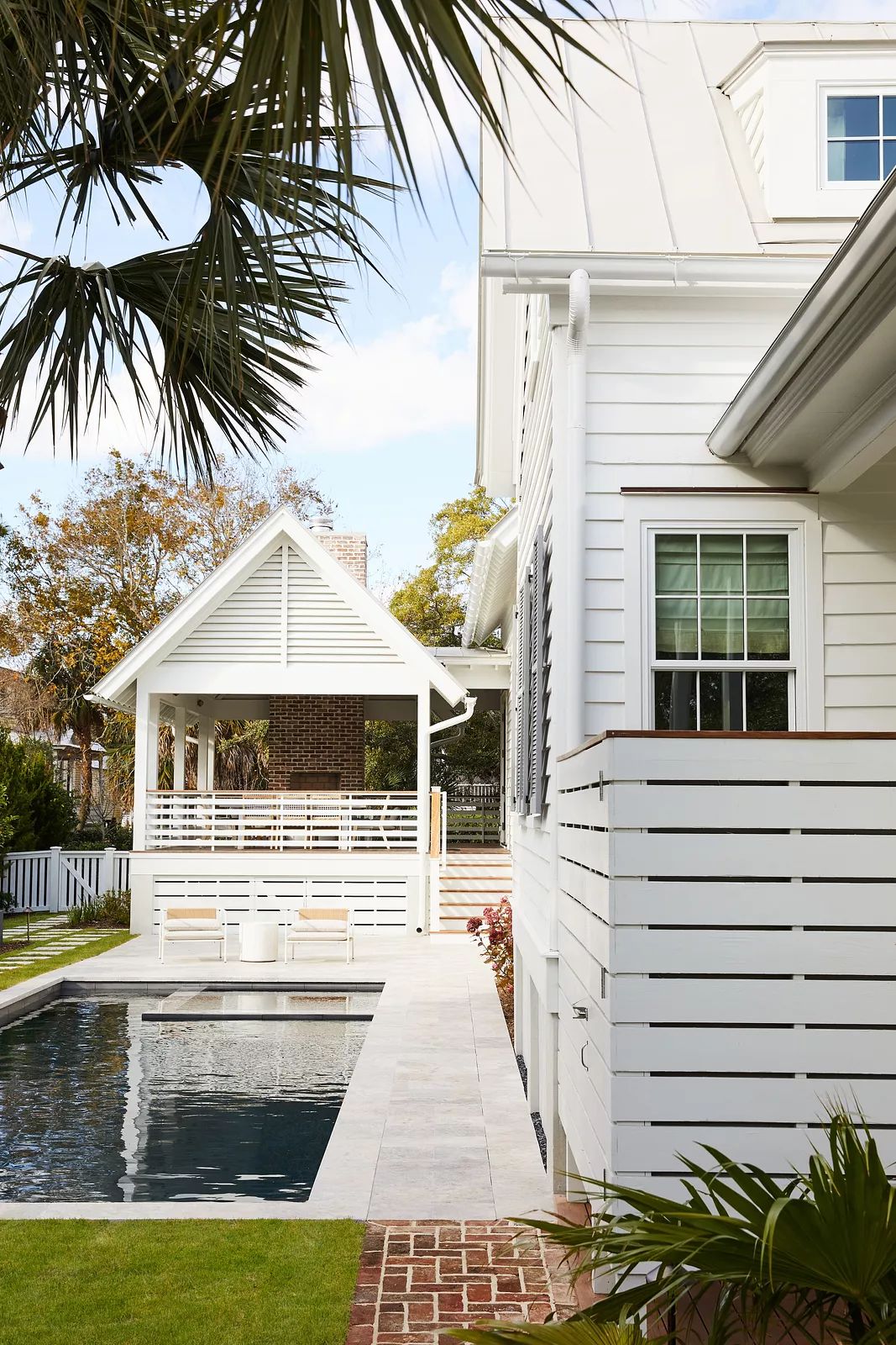 Exterior rear view with swimming pool, white decking, pergola, and greenery including palm trees.