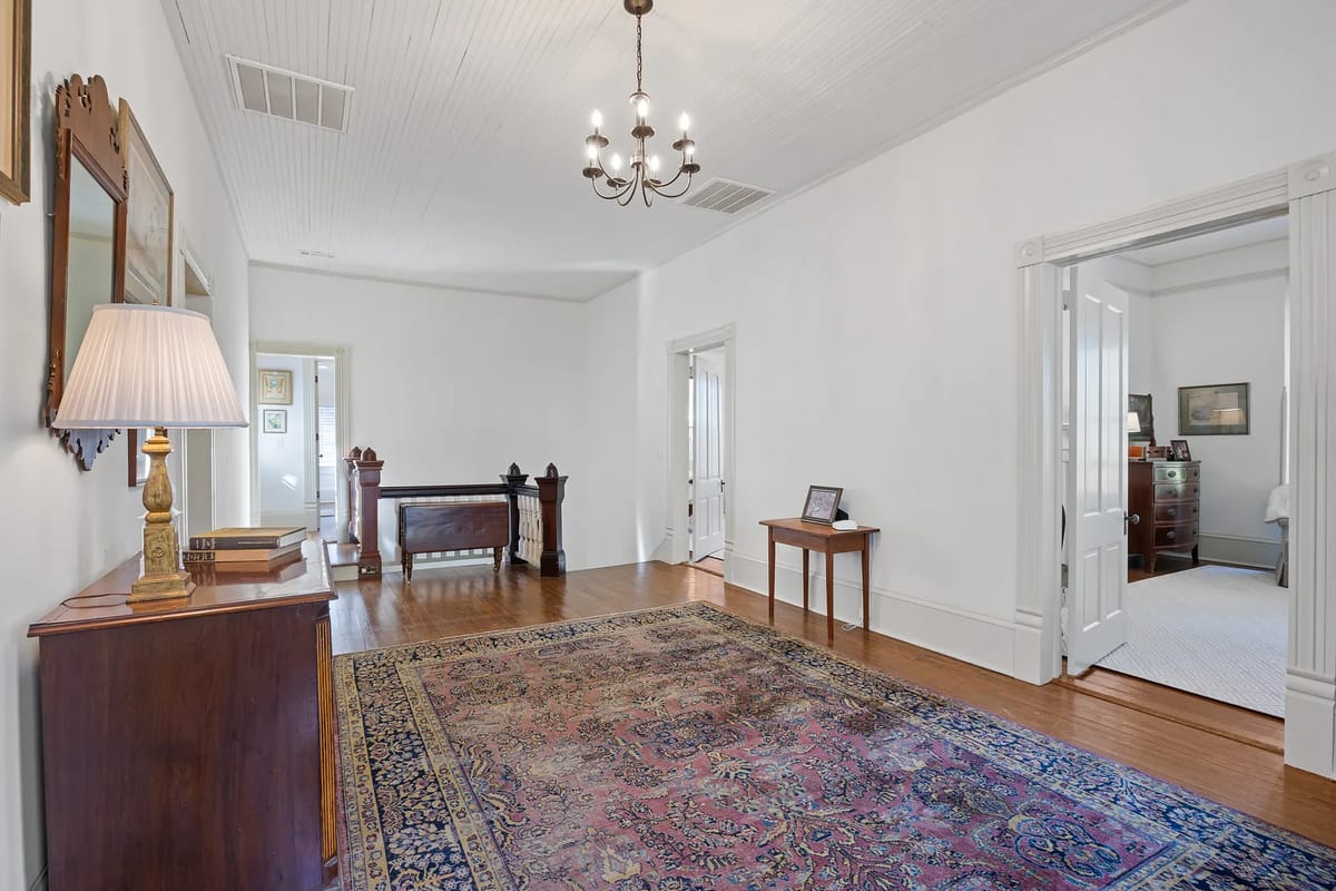 Hallway with patterned rug, wooden console table, chandelier, and two doors to adjacent rooms.