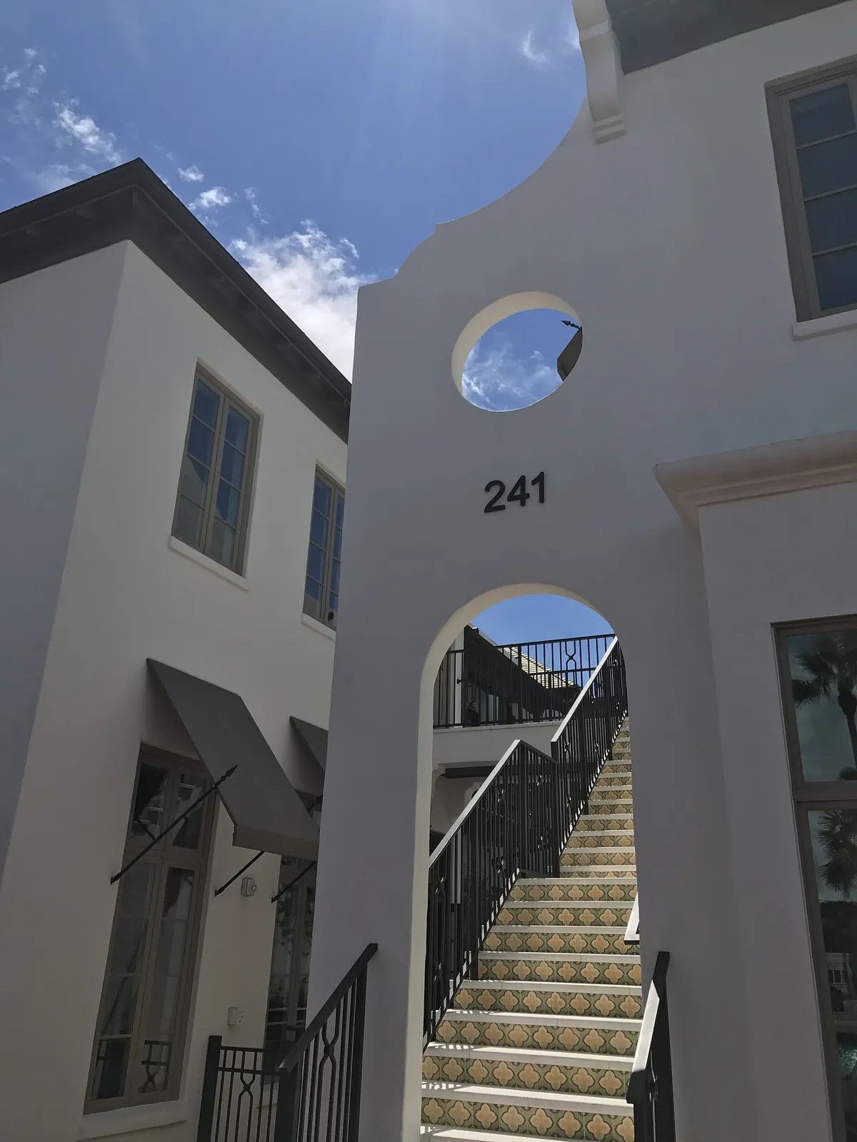 Exterior front view with white building, archway, stairs, patterned tiles, and clear sky.