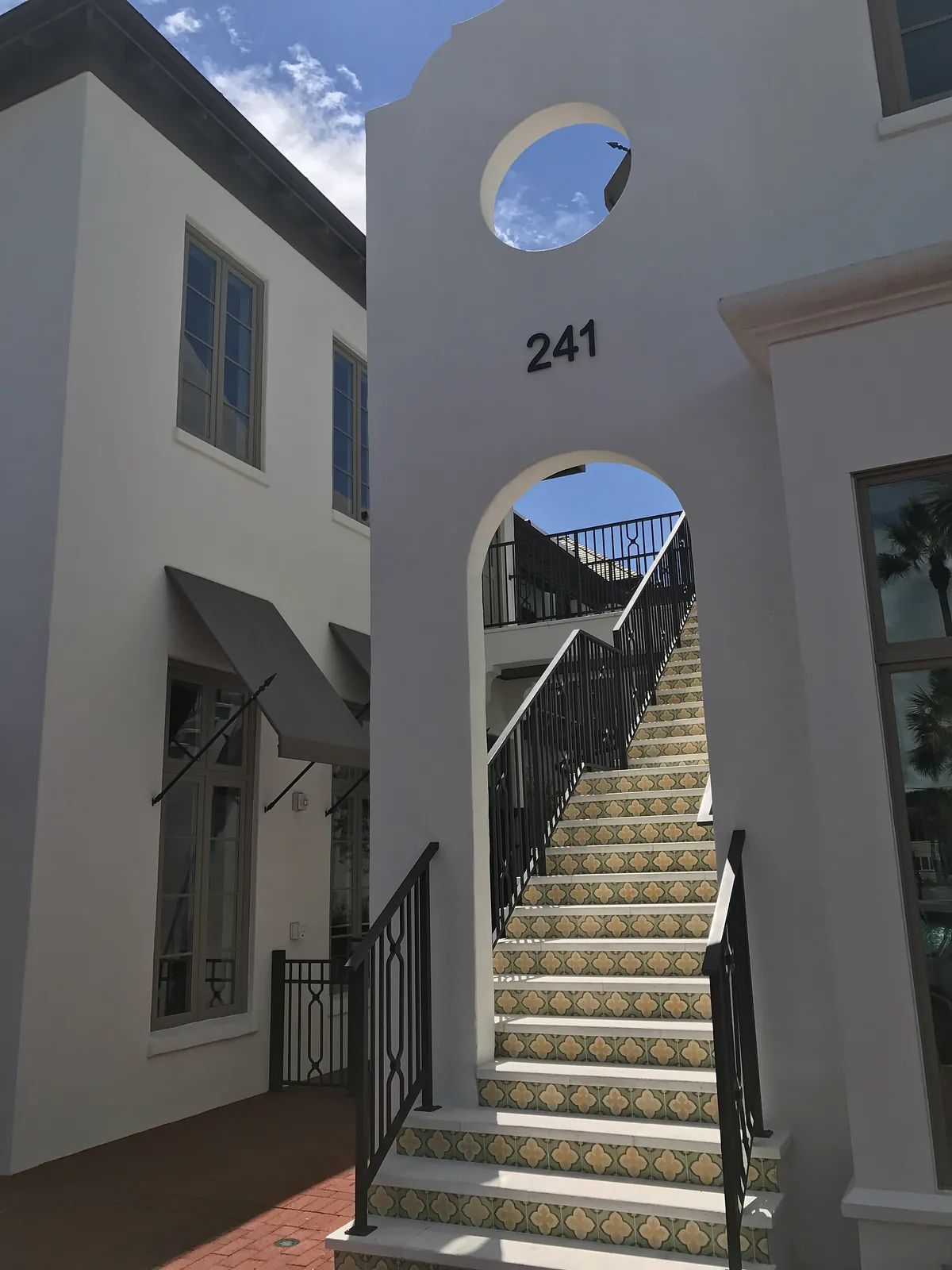 Exterior front view with a staircase, arched door, sign '241', and patterned tiles.