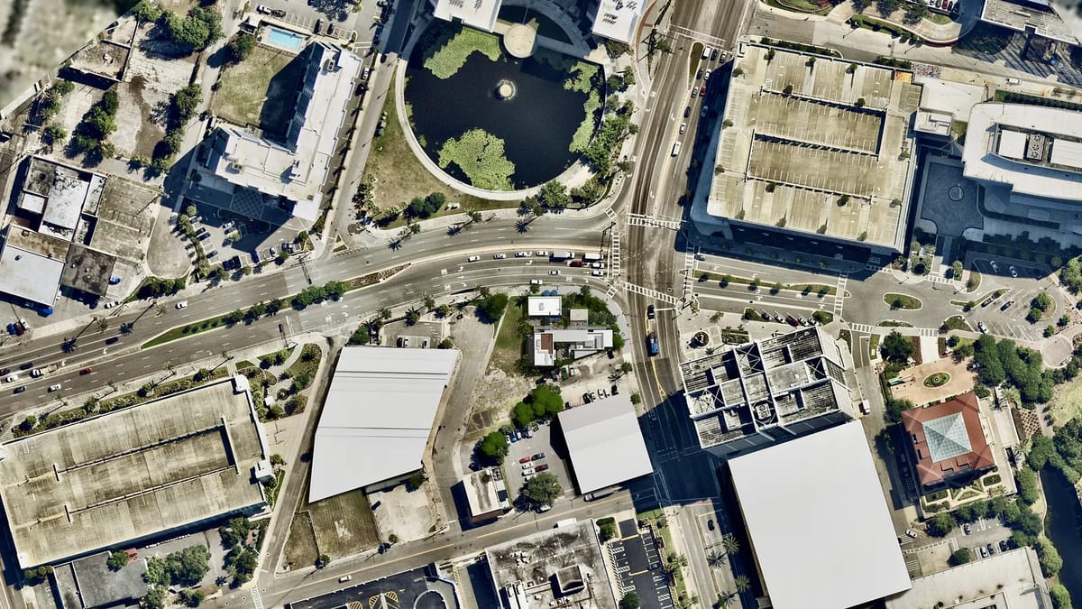 Aerial view of a city intersection with roads, buildings, and a circular pond.