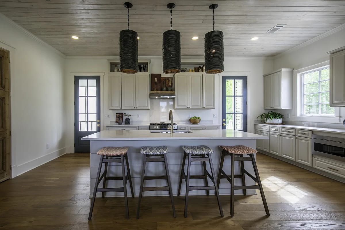 Kitchen with large island, stools, white cabinetry, stainless steel stove, hardwood floor, and natural light from windows