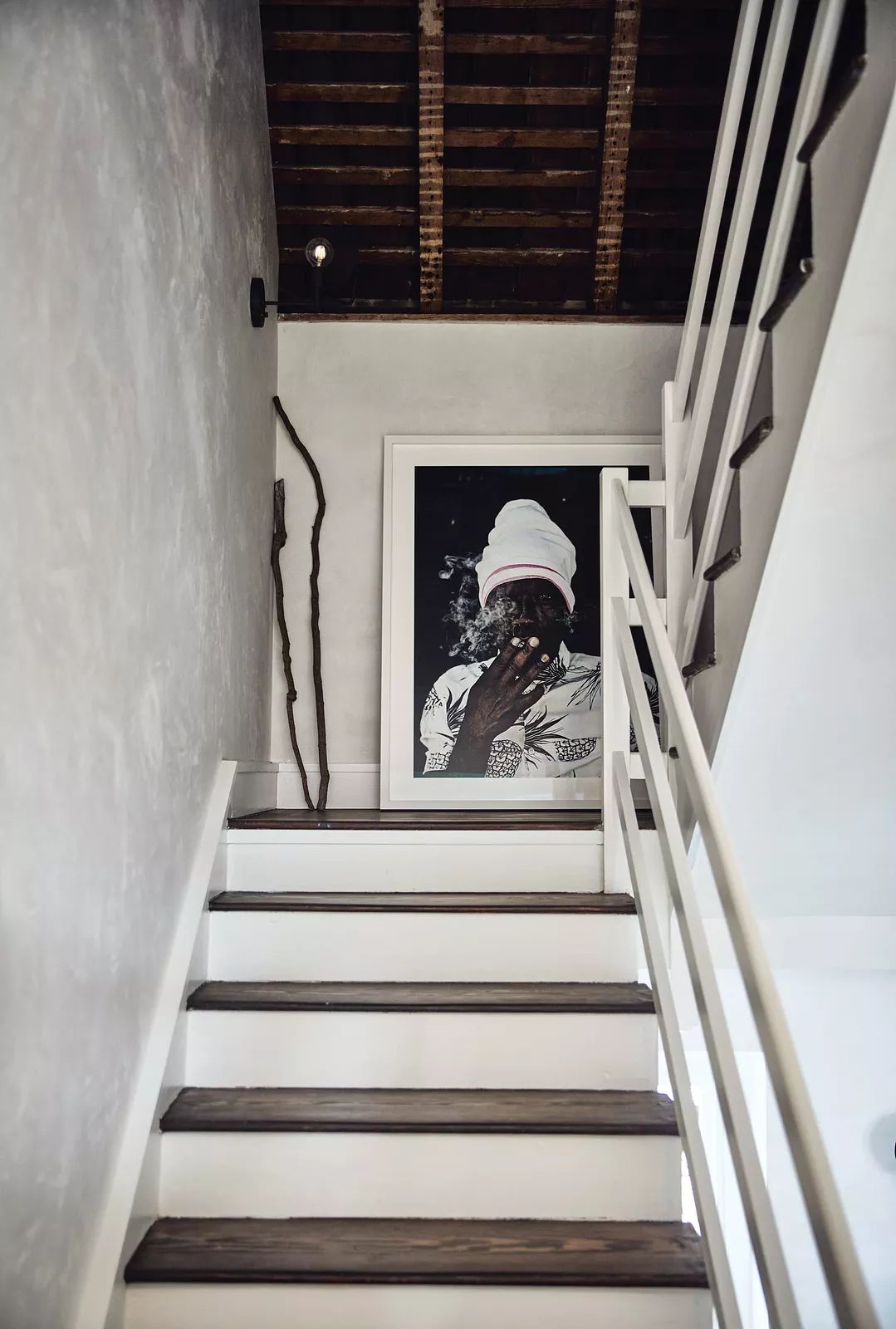 Staircase with wooden steps, black and white artwork, branch decor, and exposed wooden beams.