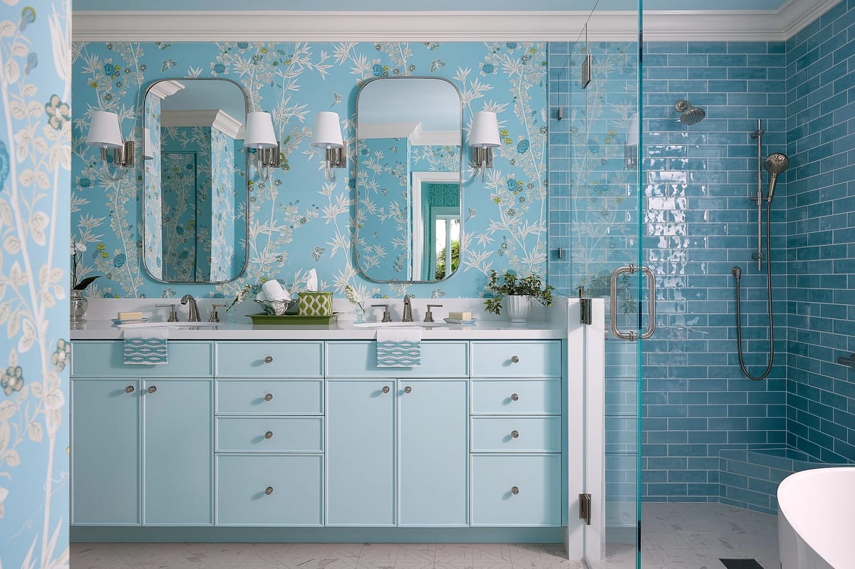 Bathroom with dual sinks, light blue cabinetry, floral wallpaper, glass shower, and freestanding bathtub.