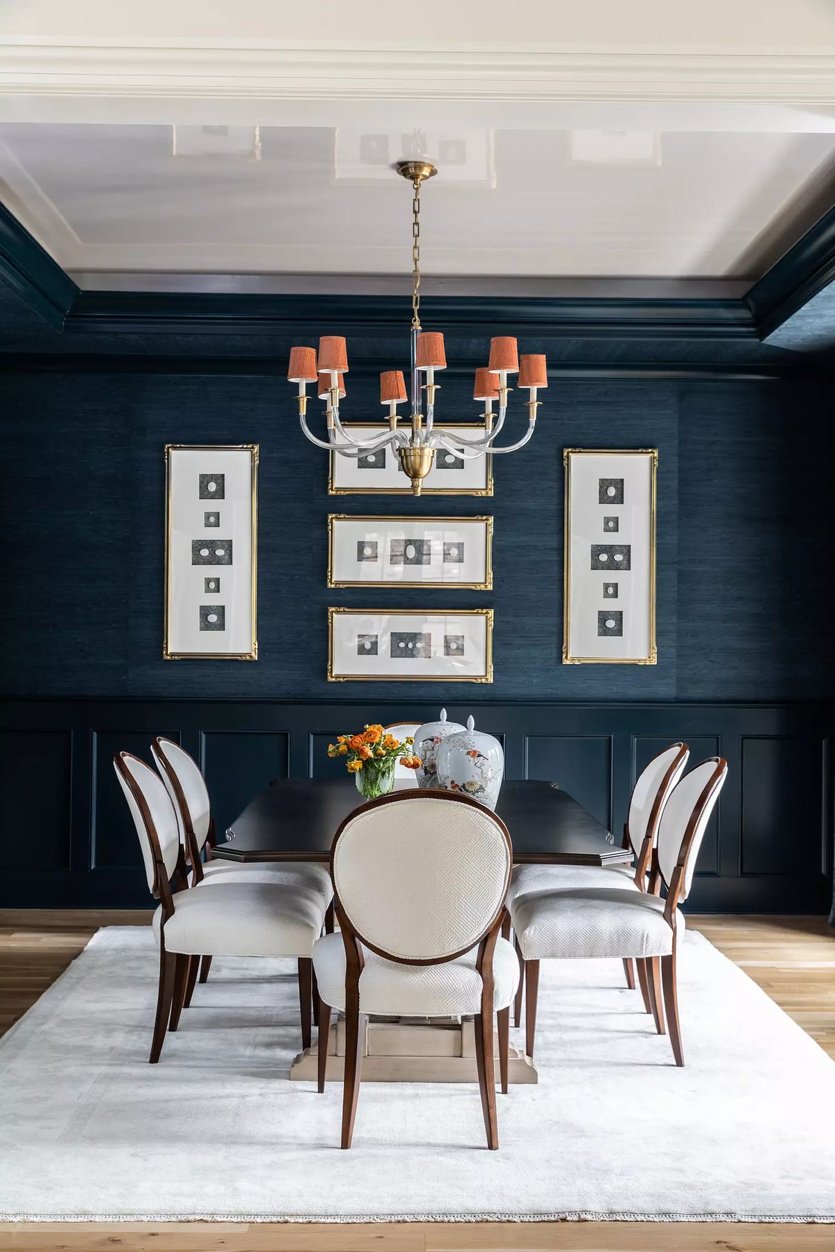 Dining room with dark wood table, six chairs, blue walls, white wainscoting, chandelier, and area rug.