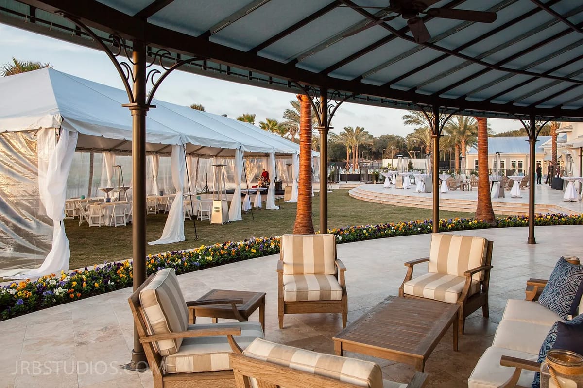 Outdoor patio with seating chairs, coffee table, large tent, and landscaped flower beds.