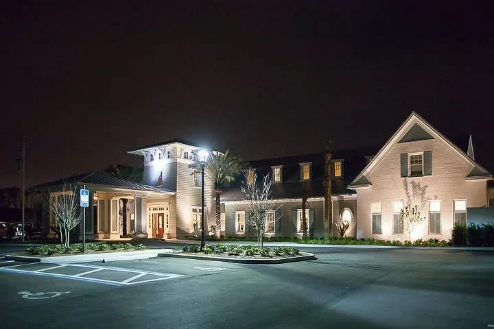 Exterior front view of a building with peaked roof, columns, entrance, and landscaped parking area.