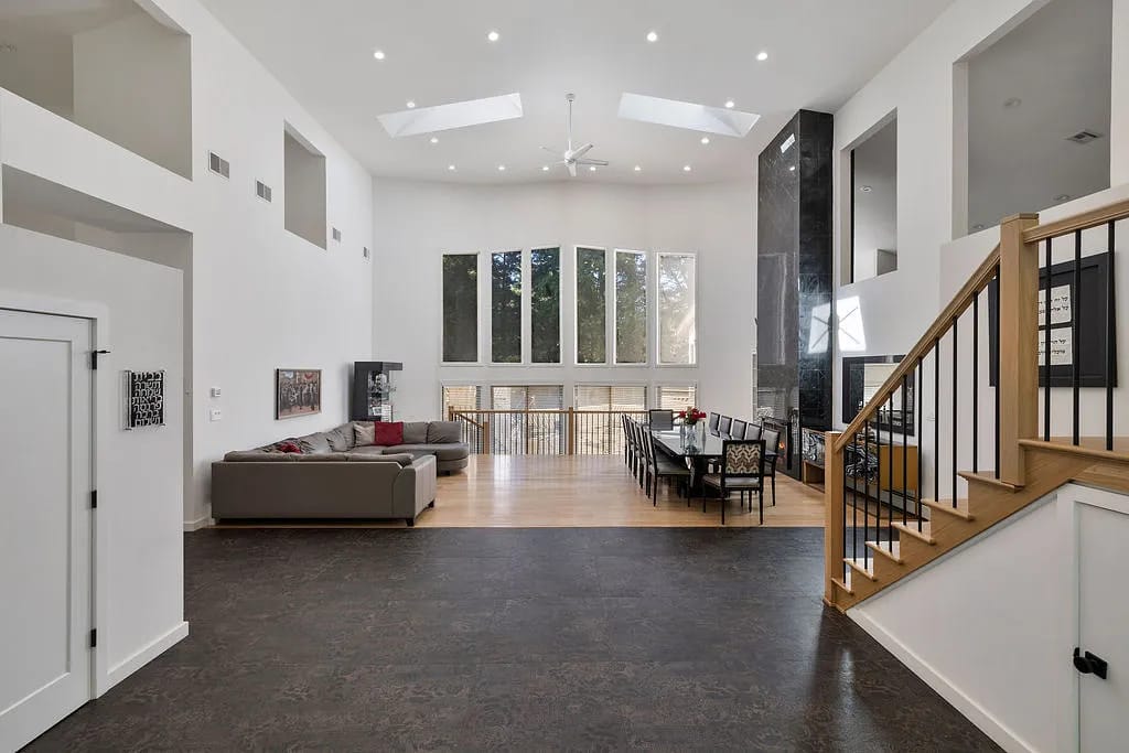 Living room with gray sectional sofa, dining table, large windows, and staircase.