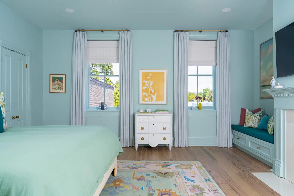Bedroom with teal wall, green bedspread, windows, white dresser, and floral area rug.