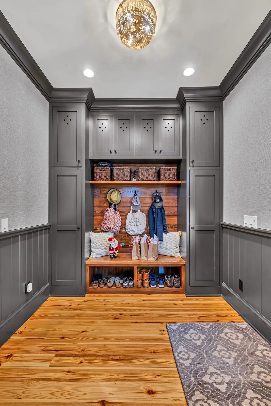 Mudroom with built-in bench, gray cabinetry, wall hooks, and patterned area rug on wooden floor