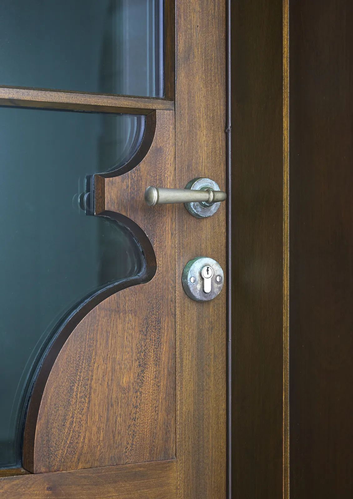 Close-up of a decorative wooden door with glass panel, handle, and lock.