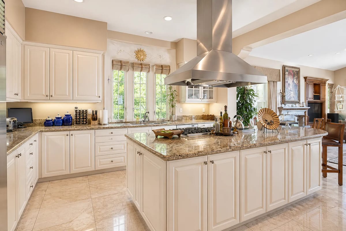 Kitchen with white cabinetry, granite island, stainless steel appliances, and a dining area in the background.