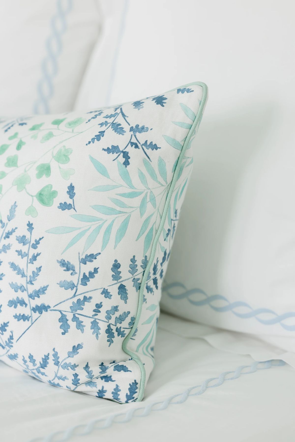 Bedroom detail with floral patterned pillow on white linens.