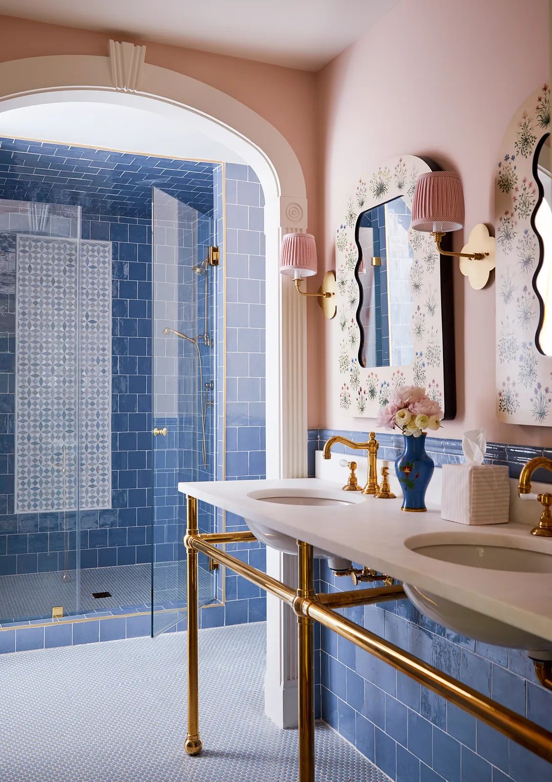 Bathroom with dual sink vanity, decorative mirrors, glass shower, and blue tiles on light pink walls