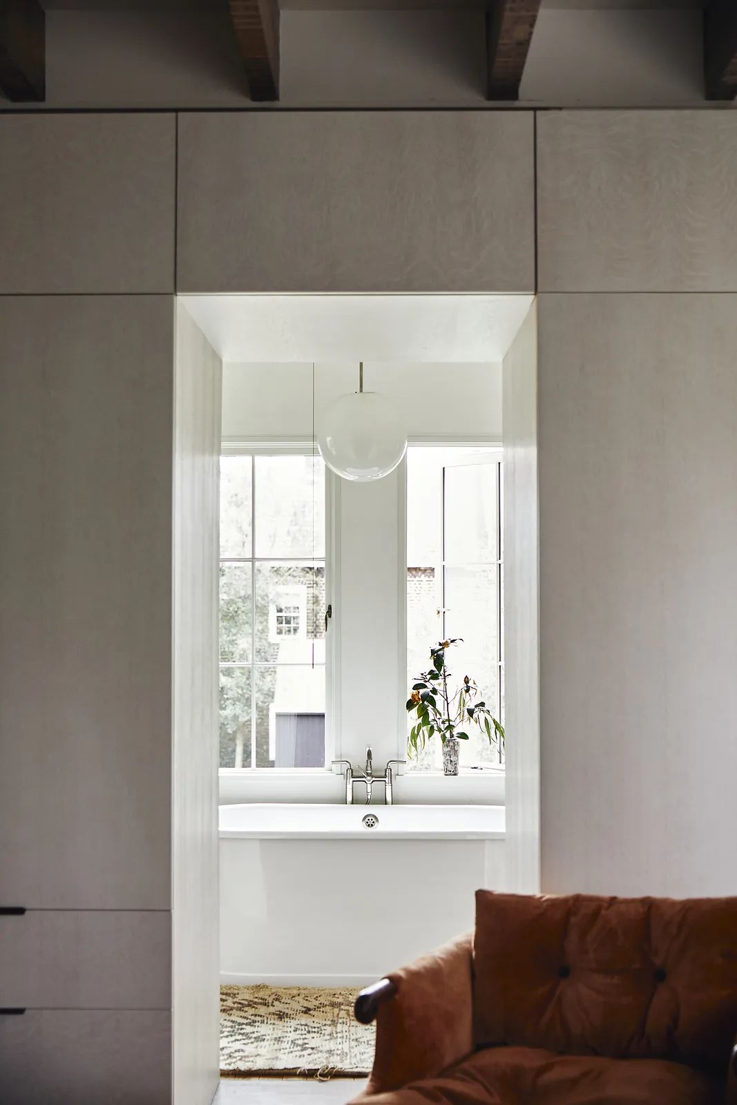 Bathroom with freestanding bathtub, large windows, wood cabinetry, and pendant light.