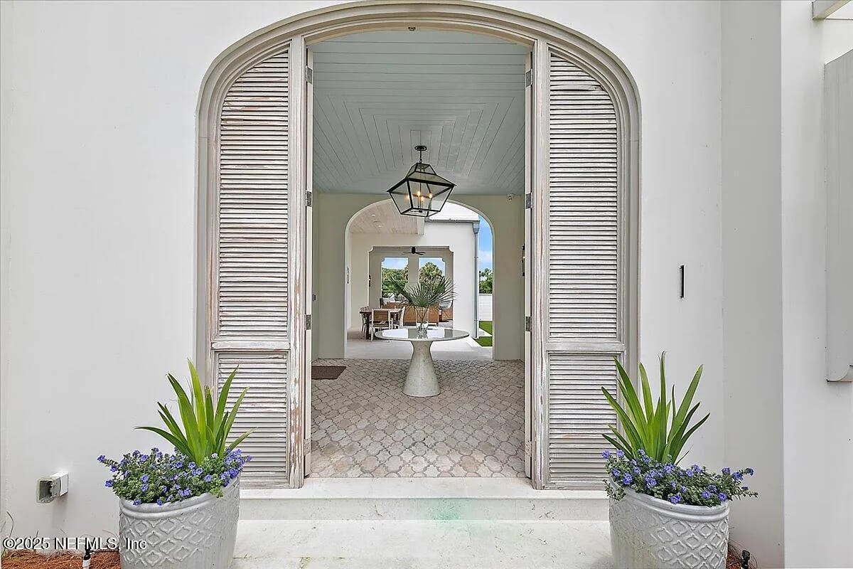 Foyer with arched doors, pendant light, planters, cobblestone floor, and panel ceiling leading to an open area.