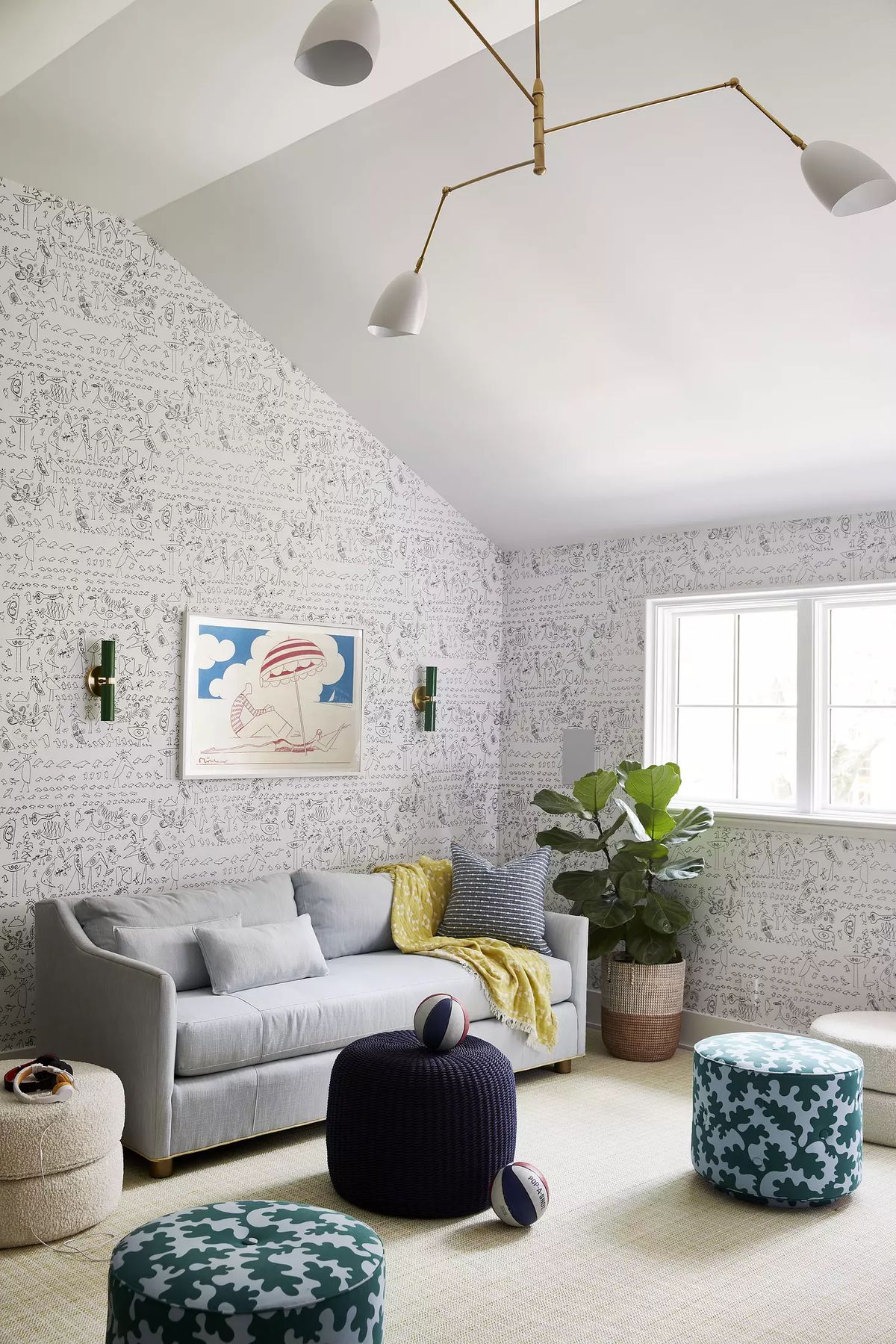 Living room with gray sofa, colorful poufs, area rug, large window, and patterned wallpaper.