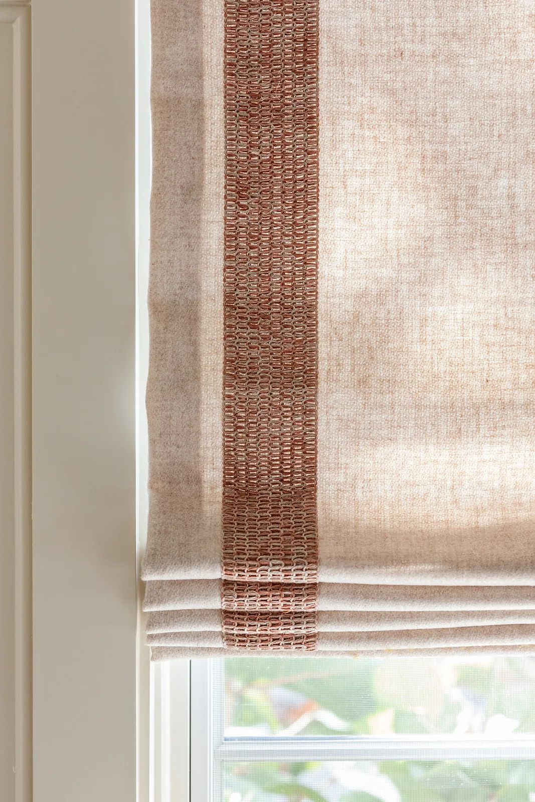 Fabric window treatment with beige material and a reddish woven stripe.