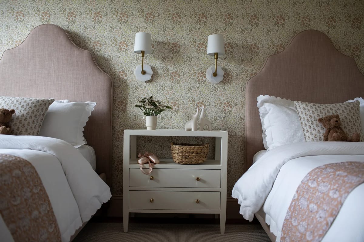 Bedroom with twin beds, pink headboards, white nightstand, floral wallpaper, and wall sconces