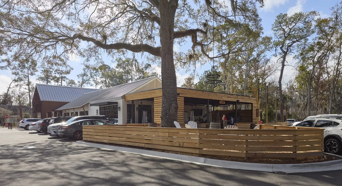 Exterior view of commercial building with wooden deck, large windows, and surrounding fence.