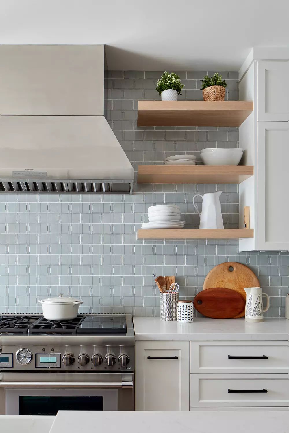 Kitchen with stainless steel oven range, open shelves, white countertops, tile backsplash, and decorative items.