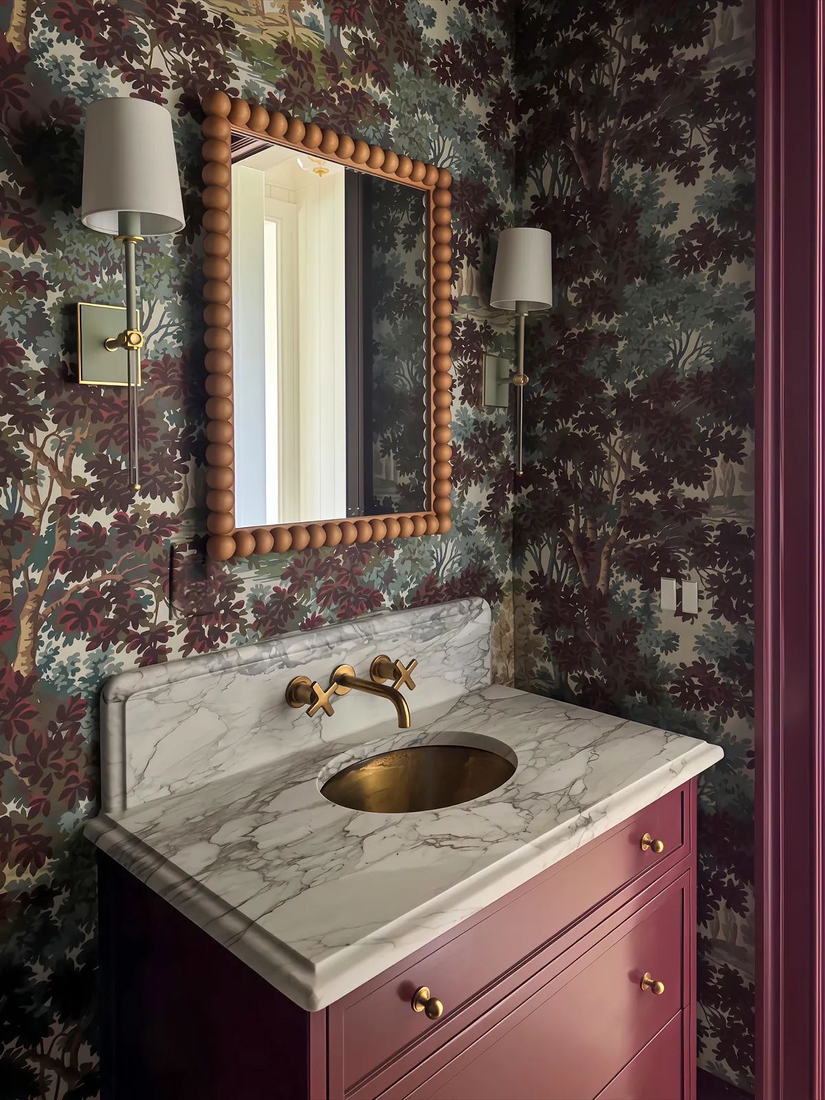 Powder room with marble countertop, circular sink, wooden cabinetry, forest wallpaper, sconces, and round mirror.