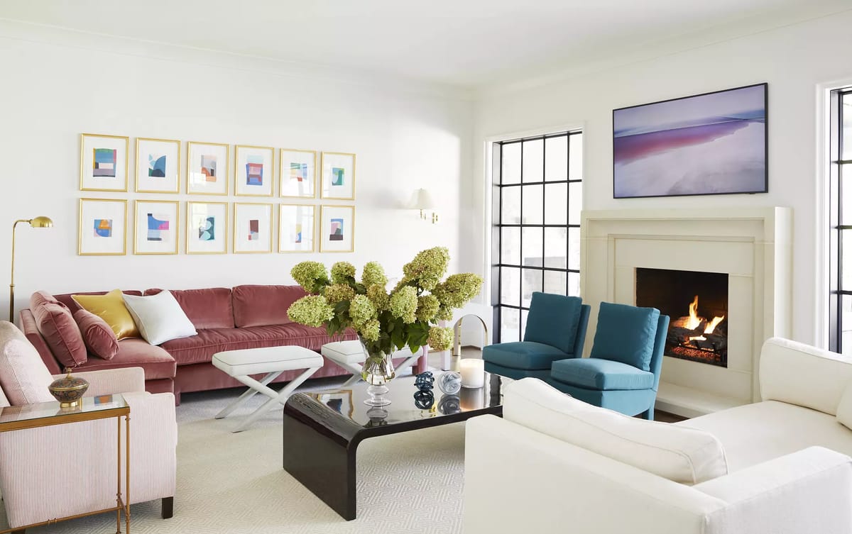 Living room with pink sofa, white armchair, teal chairs, glass coffee table, fireplace, and wall artwork.