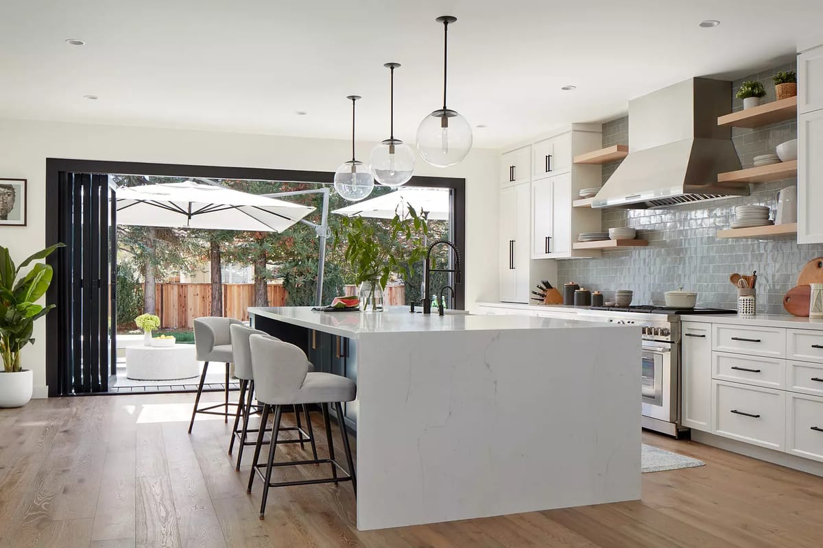 Kitchen with marble island, bar stools, stainless steel stove, open shelving, and large glass doors to patio.