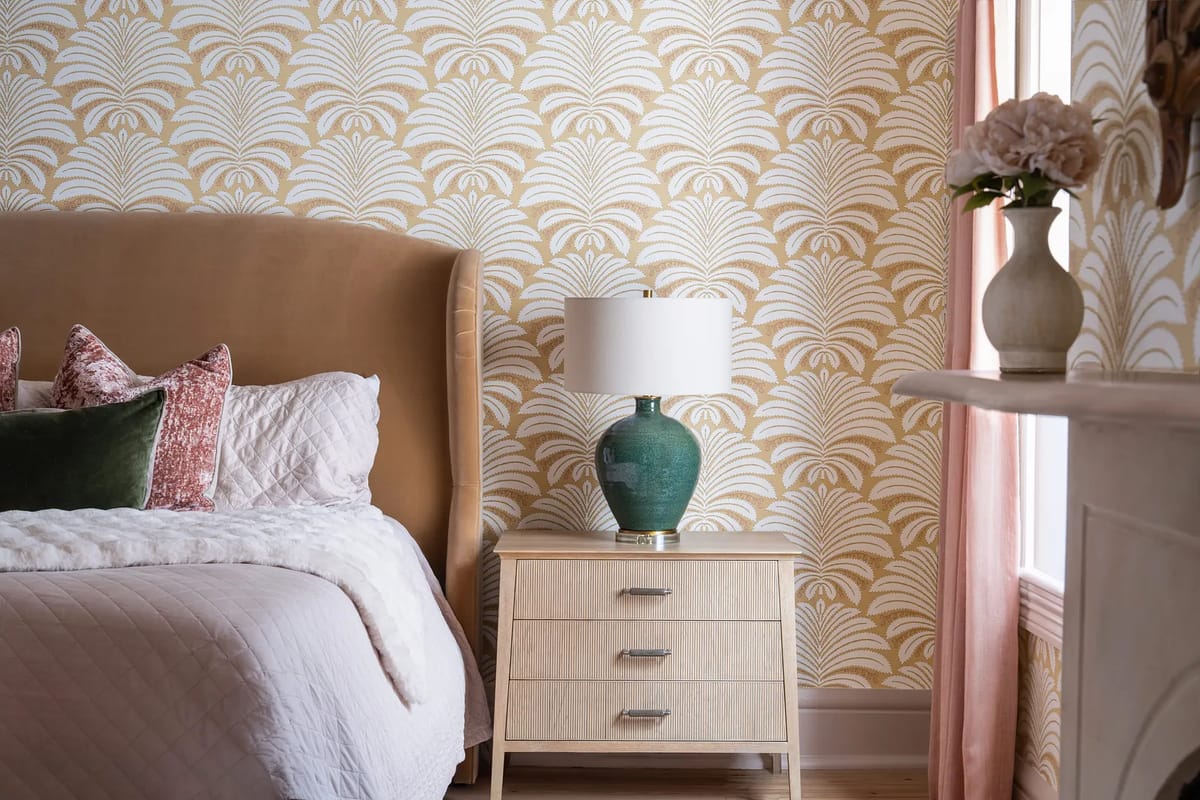 Bedroom with tufted beige headboard, quilted white bed, turquoise lamp, and patterned wallpaper.