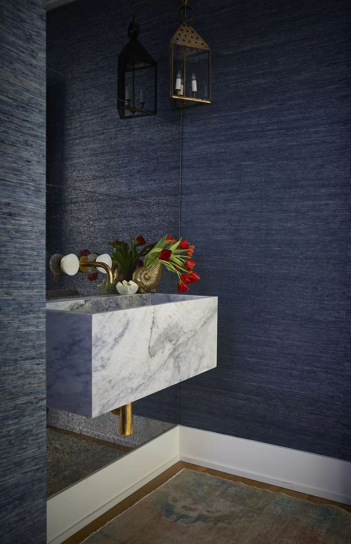 Powder room with marble sink, blue wallpaper, decorative lanterns, and vase of red flowers
