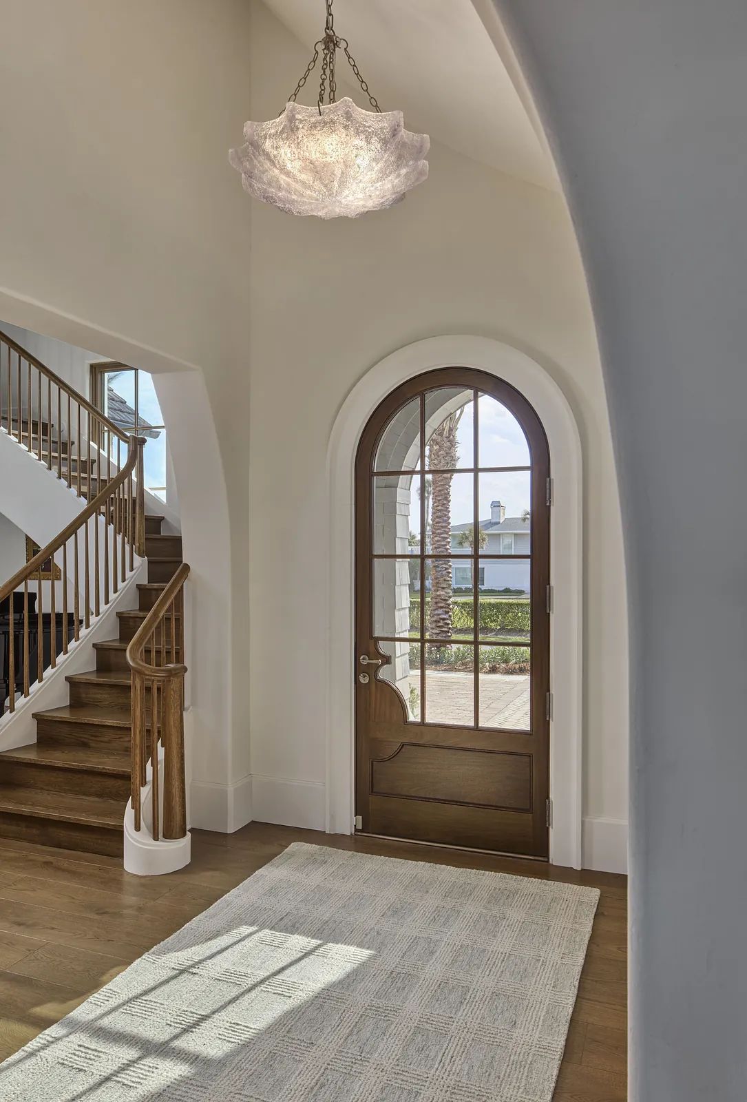 Foyer with curved staircase, arched wooden door, area rug, and white walls.