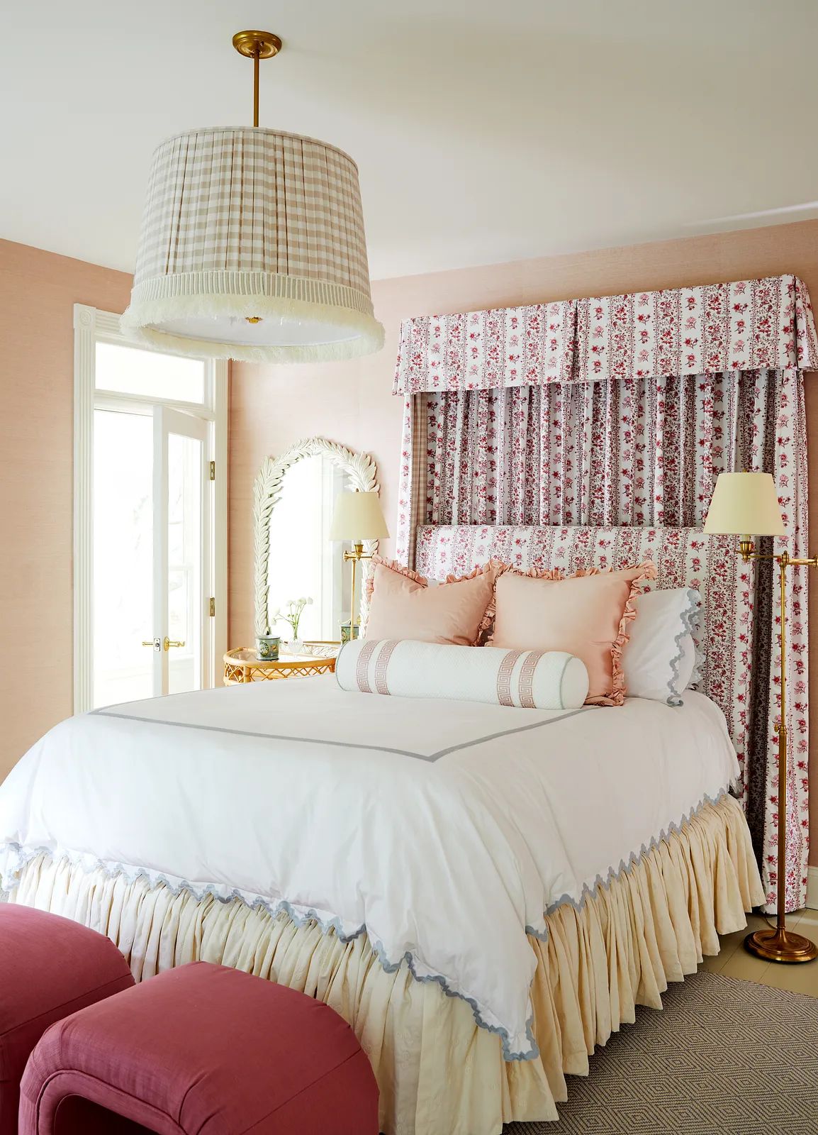 Bedroom with bed, patterned curtains, pink ottomans, round mirror, and floral canopy.