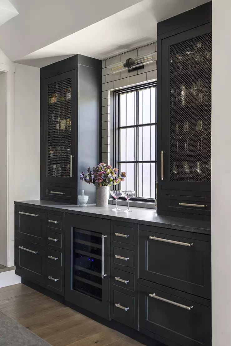 Kitchen with dark cabinetry, wine cooler, countertop, and window with metal grid detailing.