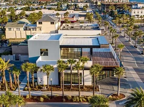 Exterior view of a modern house with flat roof, large windows, wooden deck, and palm trees.