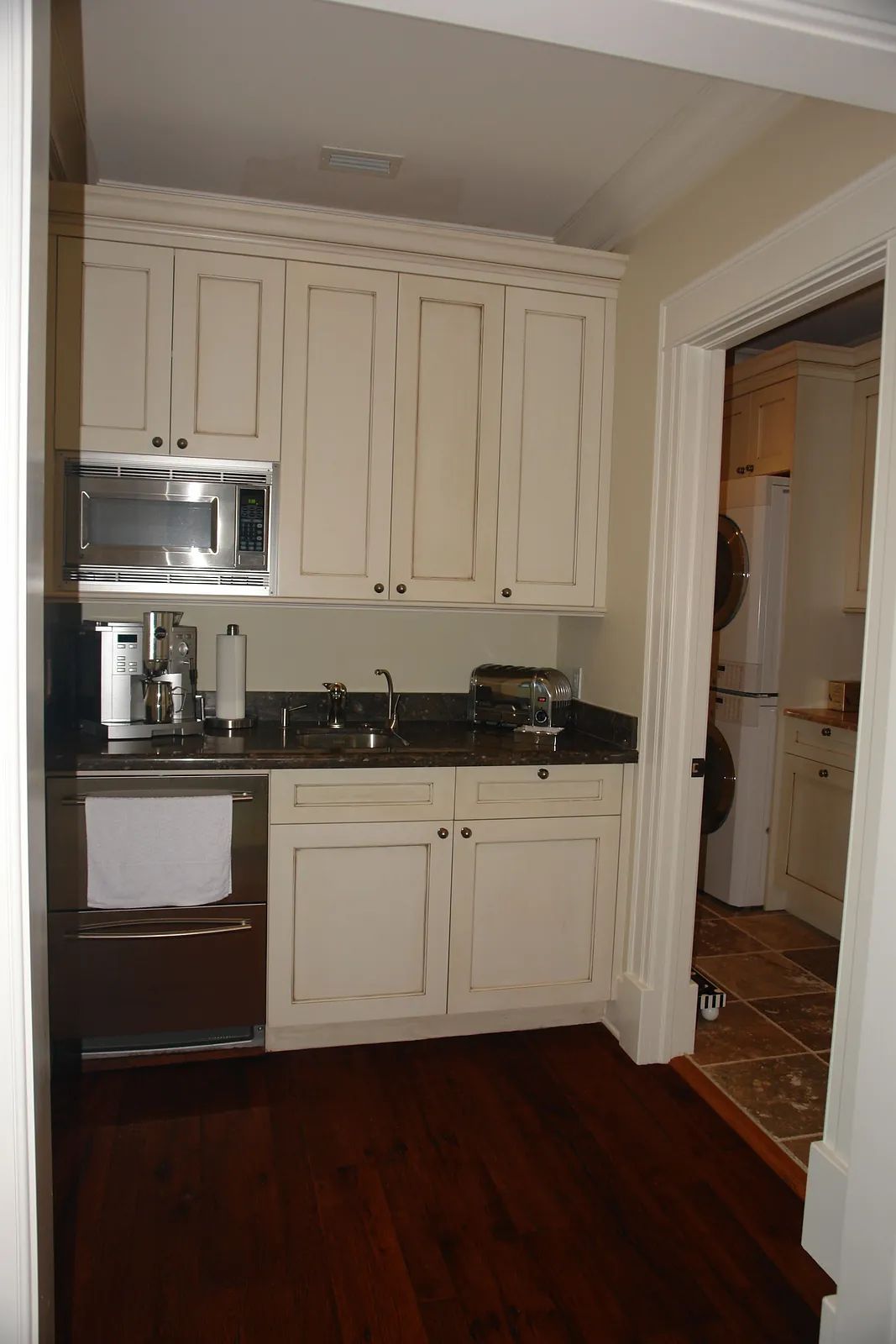 Compact kitchen with beige cabinetry, stainless steel appliances, dark granite countertop, and hardwood flooring.