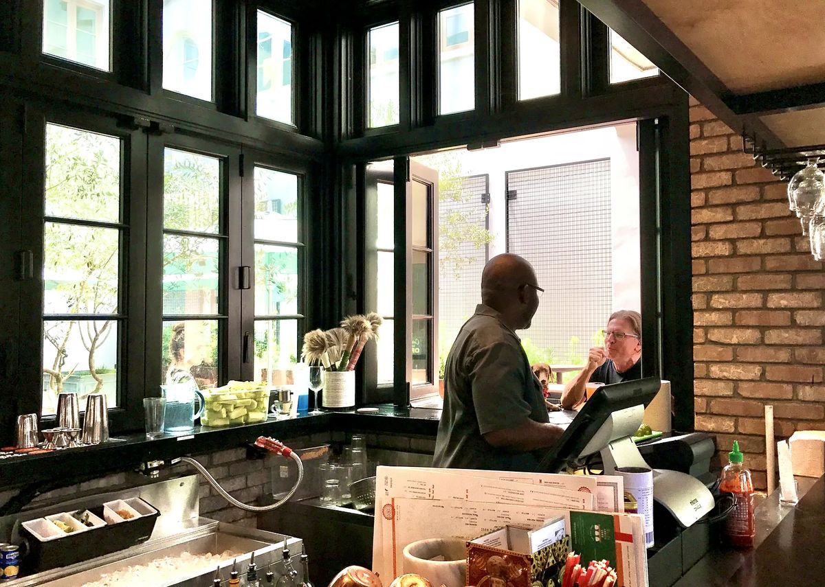 Kitchen with black countertop, brick wall, large windows, cash register, and ice bin.