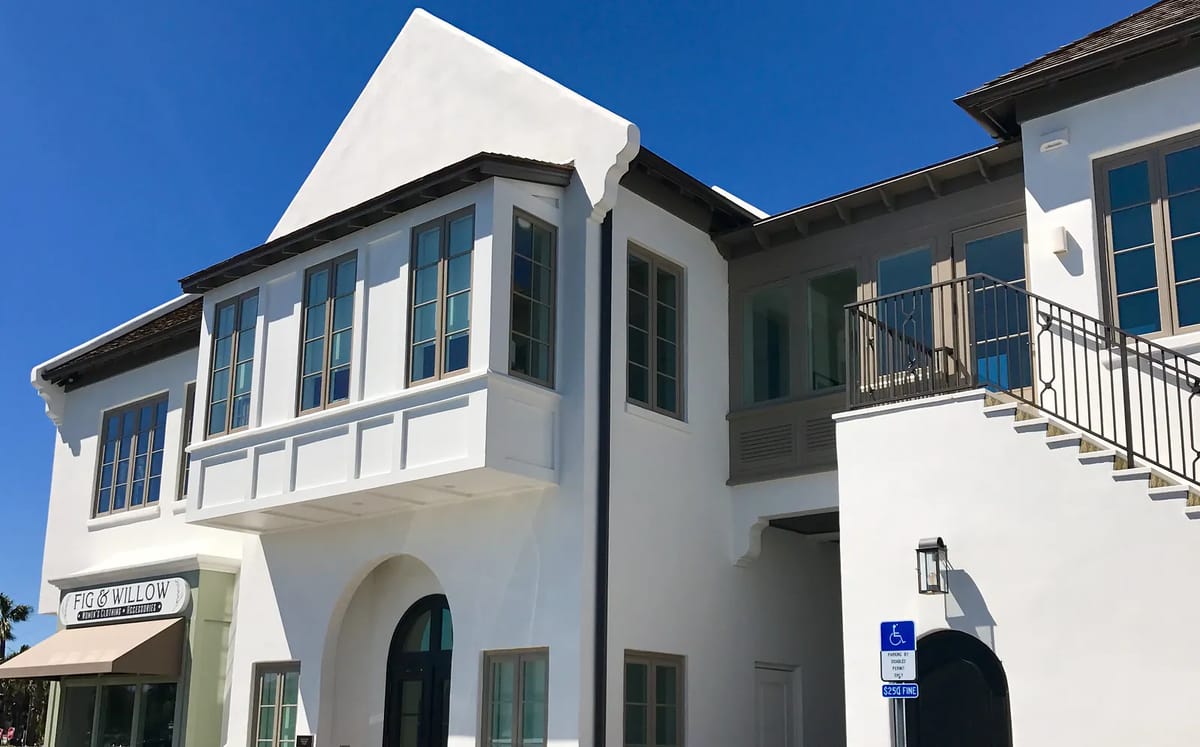 Building exterior with white stucco facade, large windows, arched doorway, and balcony.