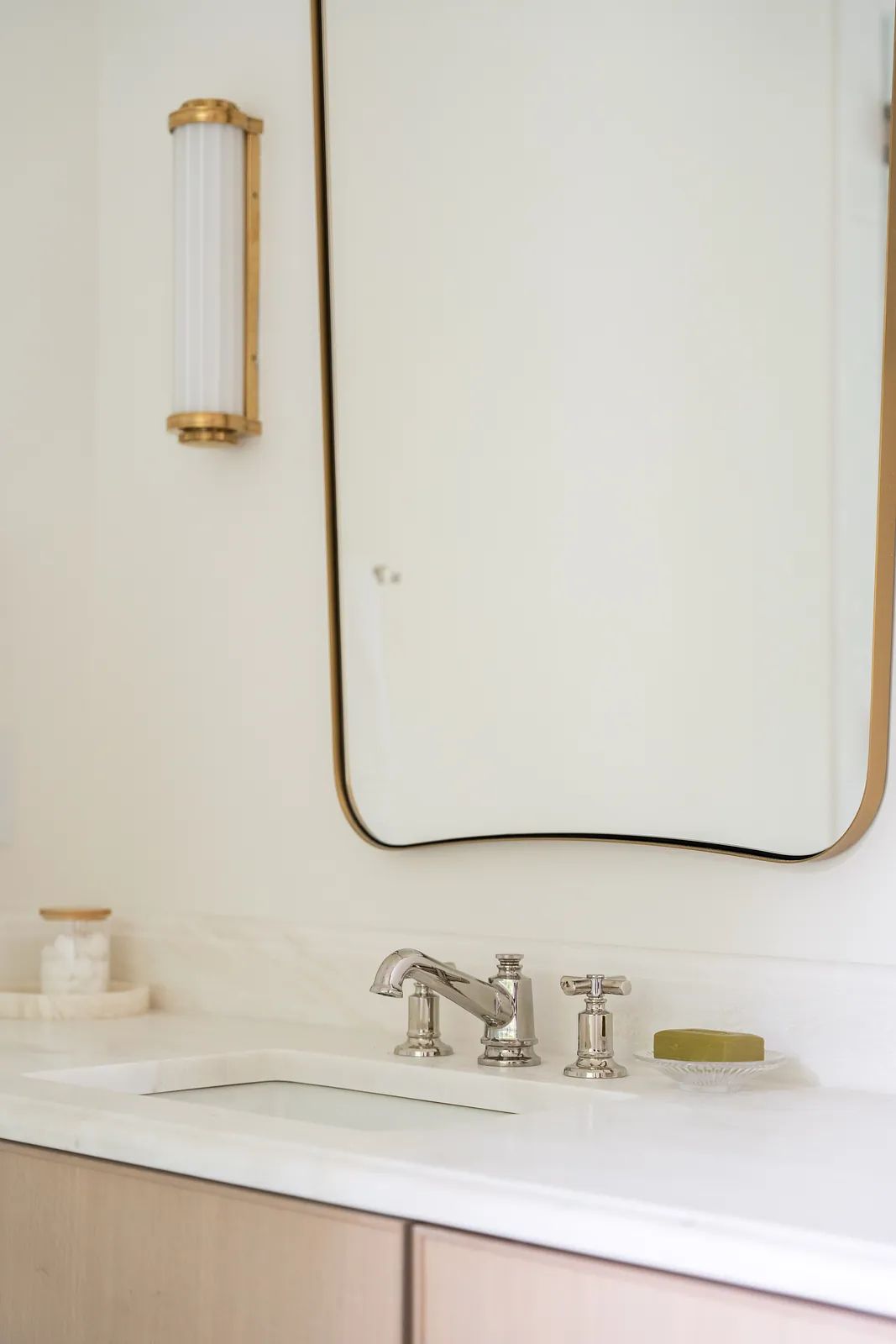 Bathroom with white countertop, chrome faucet, large gold-framed mirror, and light wood cabinetry.