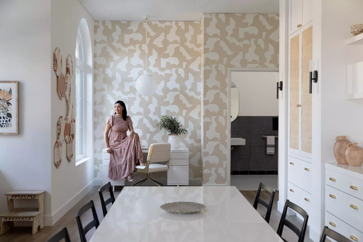 Dining room with black table, chairs, patterned wallpaper, white cabinet, and decorative items.