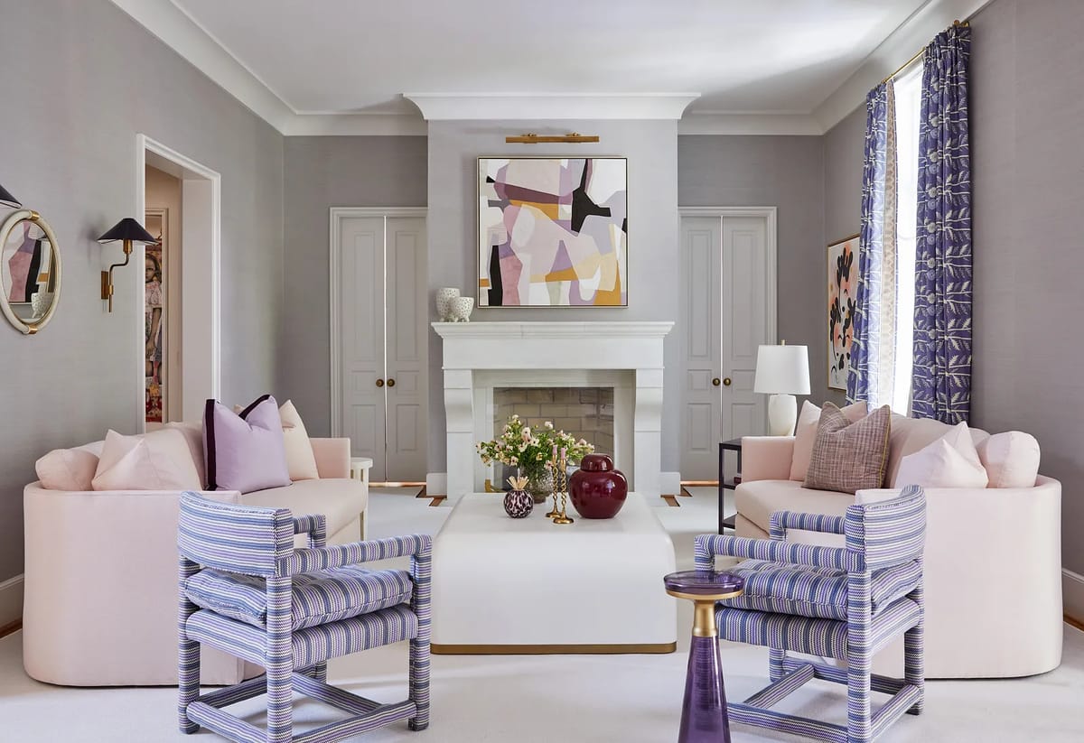 Living room with pink sofas, striped armchairs, coffee table, fireplace, artwork, and patterned curtains