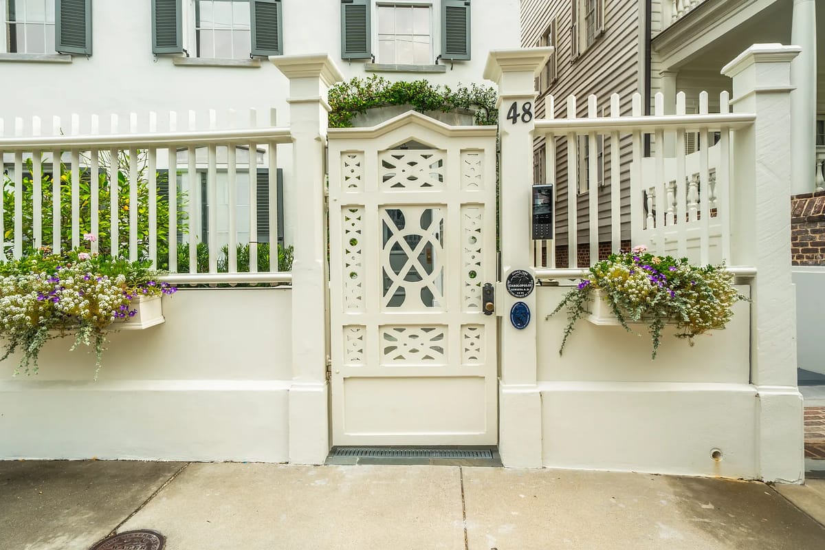 Exterior front with white decorative fence, gate, planters, and stone pathway.