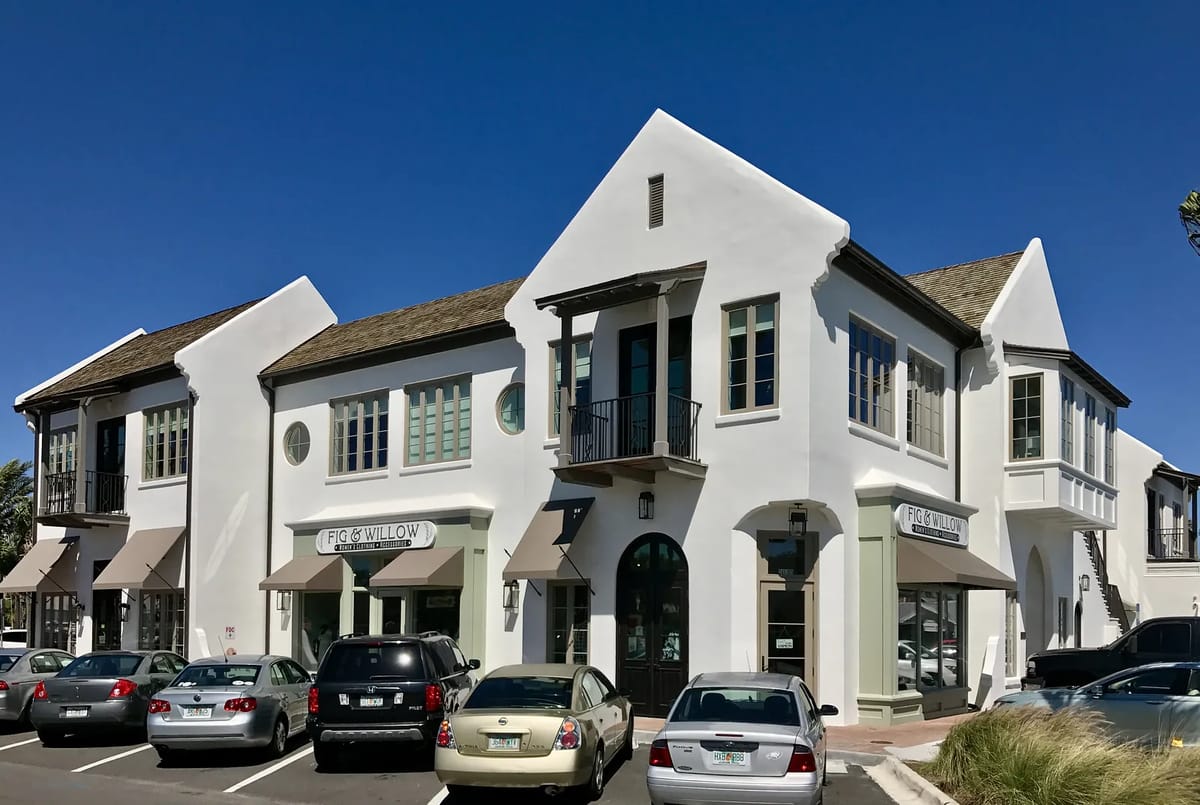 Commercial building with stucco facade, large windows, and a tile roof, surrounded by parked cars.