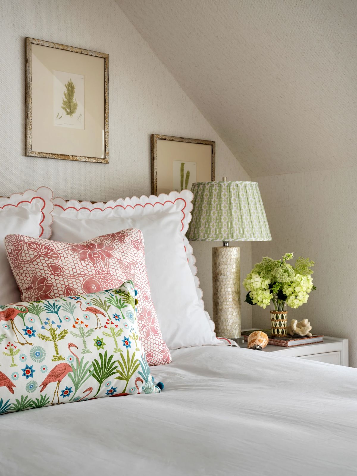 Bedroom with white linens, decorative pillows, nightstand, table lamp, and floral artwork.