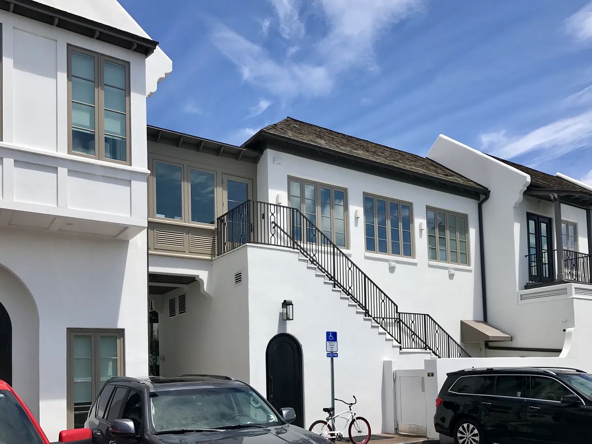 Exterior front of a building with white walls, large windows, stairs, and parked cars.