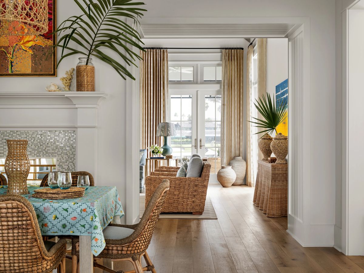 Dining room with round table, wicker chairs, artwork, fireplace, and large window.