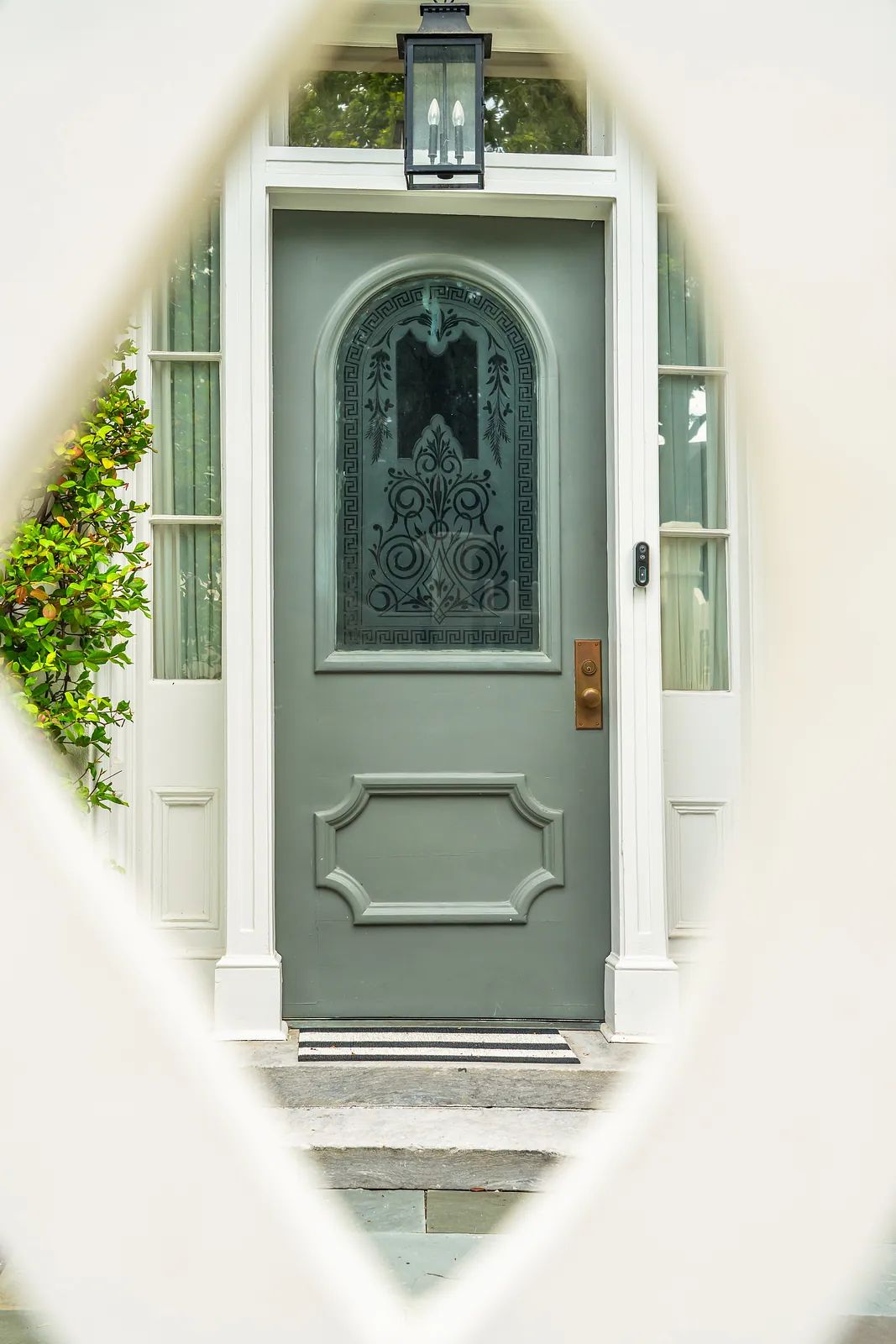 Exterior front entrance with a green door, sidelights, stone flooring, and a decorative light fixture.