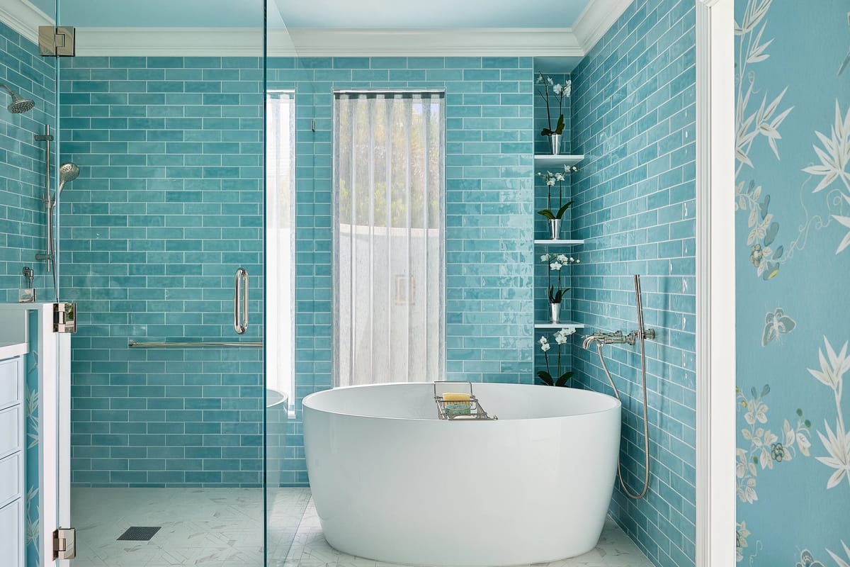 Bathroom with freestanding white bathtub, turquoise tiles, glass shower, and floral-patterned wall.